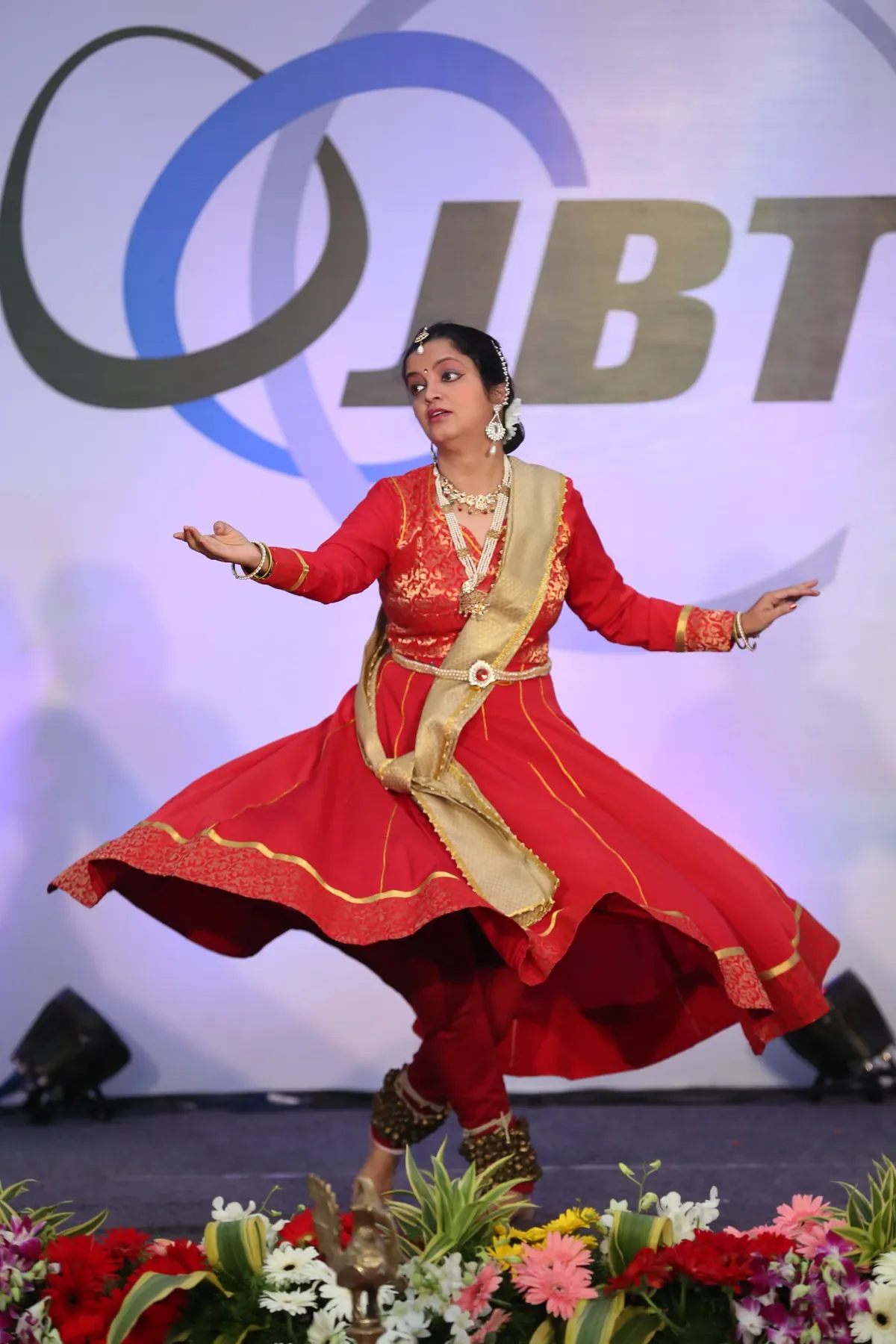 A Kathak dancer of Archana Nrityalaya with arms open and skirt in full flare on a corporate stage