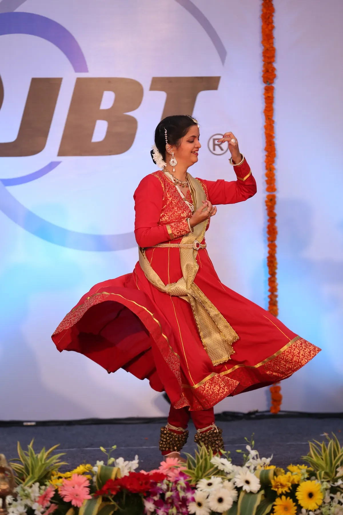 A dancer of Archana Nrityalaya mid-turn in red and gold, skirt flaring, on a corporate stage in Pune