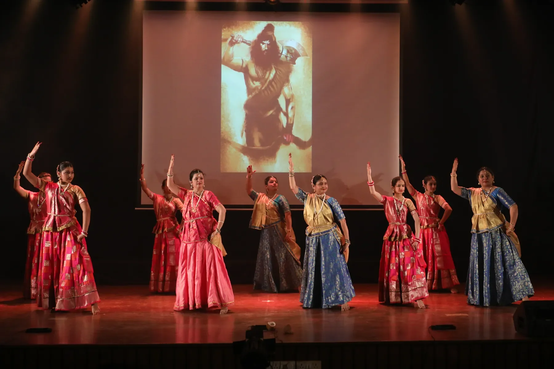 Adult students of Archana Nrityalaya dancing in a line beneath a projected image of Shiva
