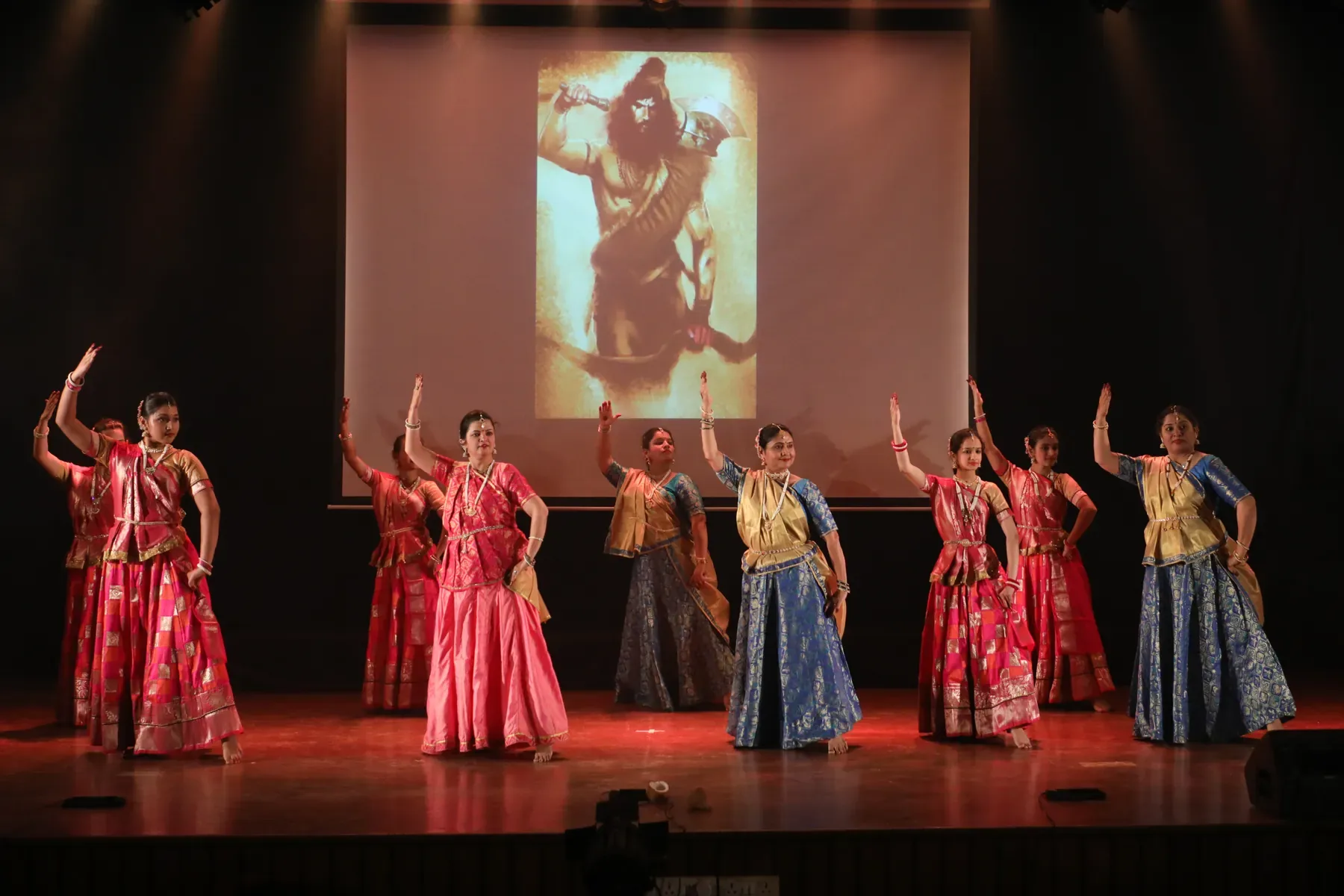 Adult students of Archana Nrityalaya dancing in a line beneath a projected image of Shiva