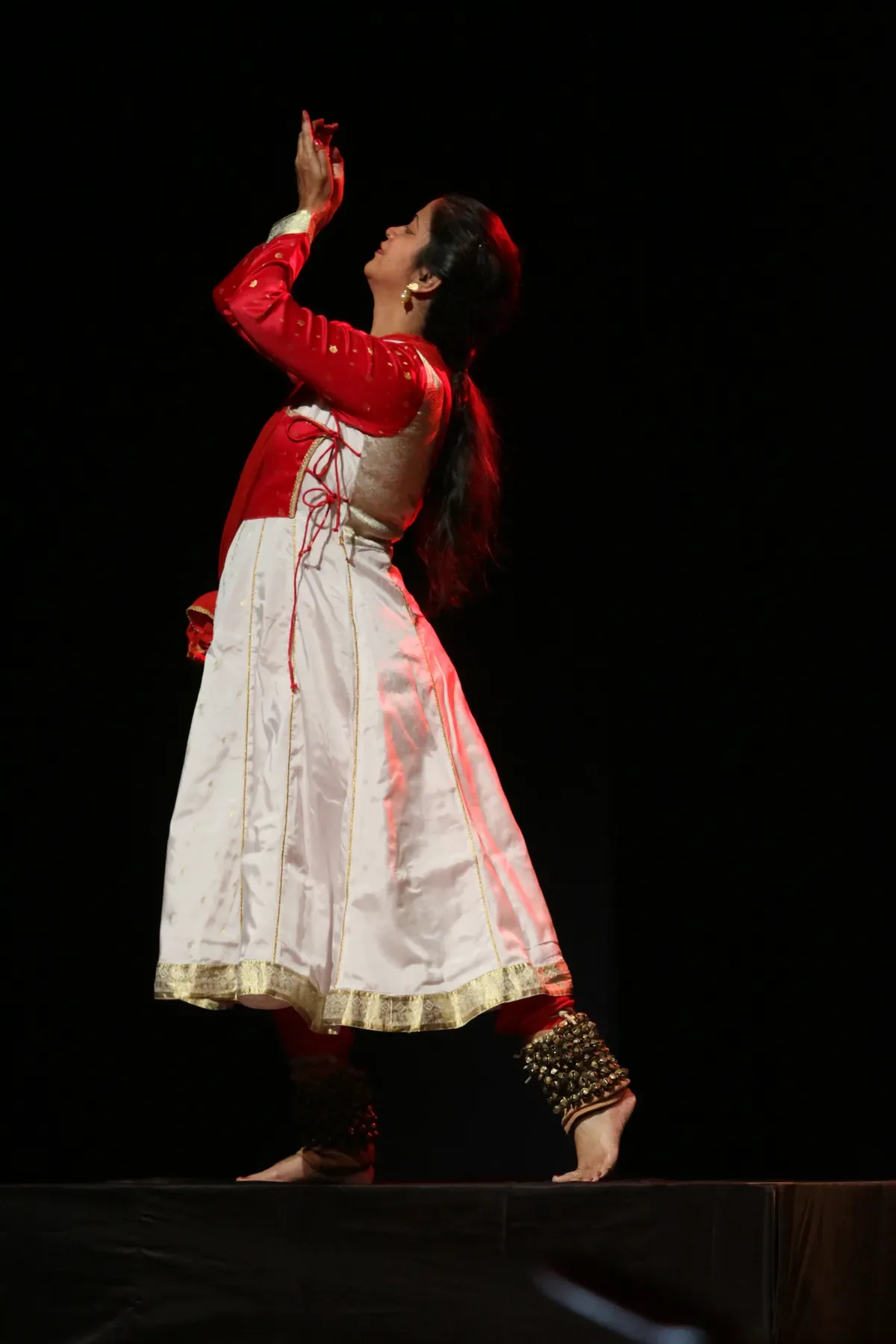 Guru Archana Patwardhan performing Kathak in Pune, one arm lifted in an invocation on a darkened stage